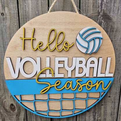 Round wood door sign with light stained background and "Hello Volleyball Season" text. The sign also features a ball and net. The sign is hanging by twine on a fence.