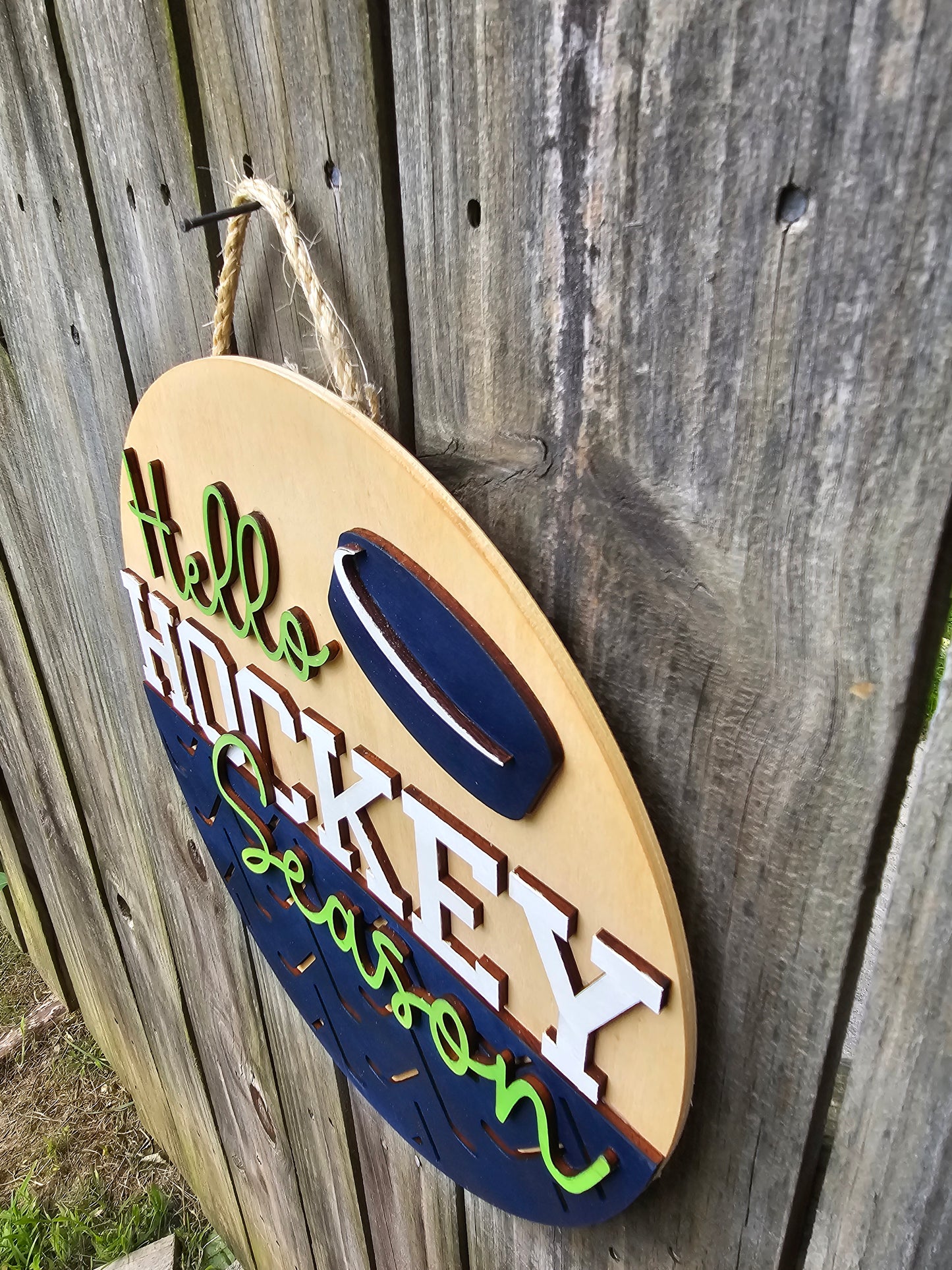 Round wooden sign with 'Hello Hockey Season' text and hockey puck design on a wooden background. This photo is taken from an angle to show off 3D elements.