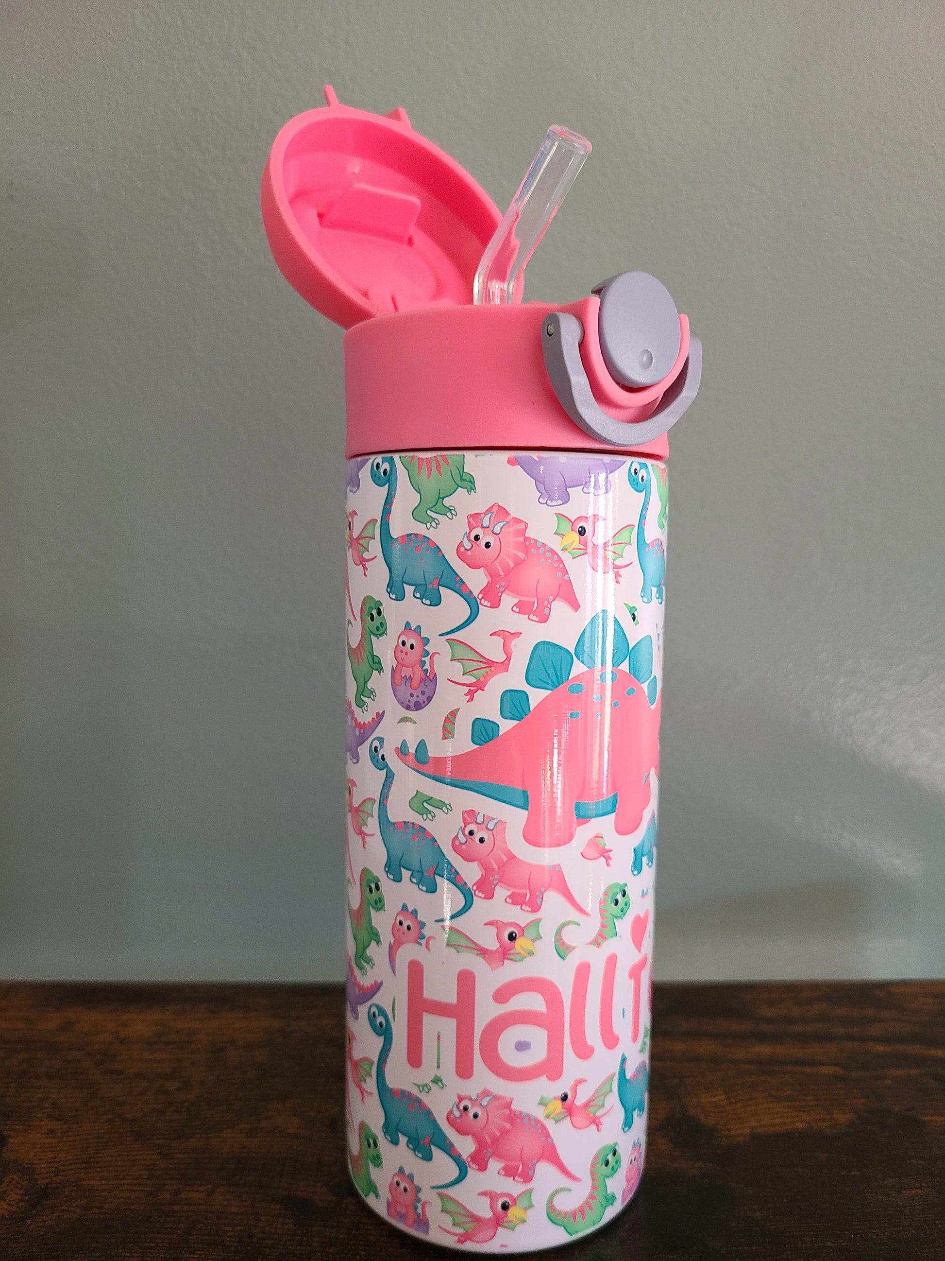 12 oz water bottle with pink lid that has a built in straw, locking push button and handle. This design features pastel rainbow dinosaurs. Personalized in coordinating colors. Back to School.