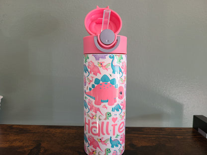 12 oz water bottle with pink lid that has a built in straw, locking push button and handle. This design features pastel rainbow dinosaurs. Personalized in coordinating colors. Back to School. Lid is open showing silicon straw