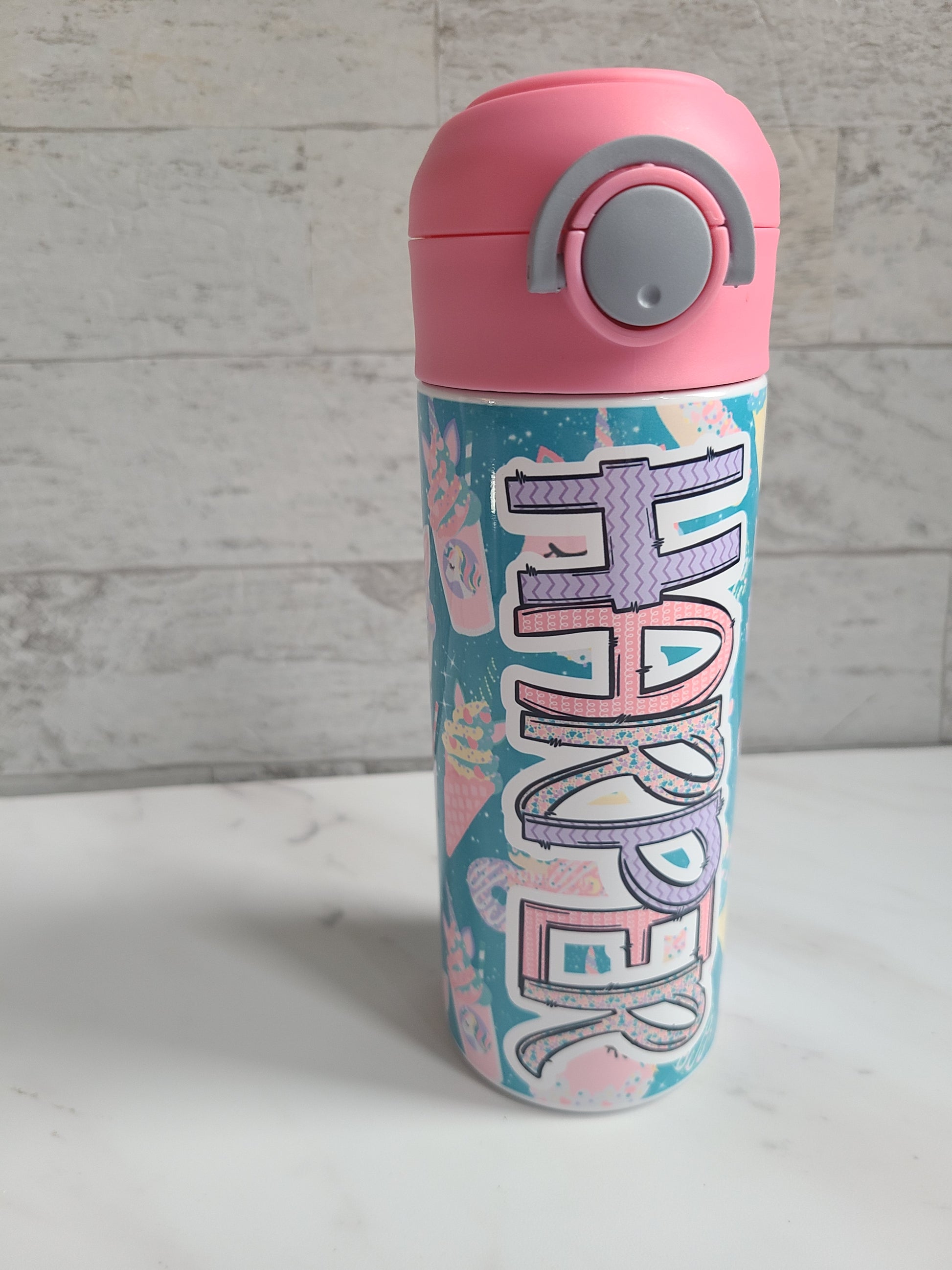 12 oz water bottle with pink lid that has a built-in straw, locking push button and handle. This design features pastel unicorn cupcakes and ice cream cones. Personalized in coordinating colors. Back to School.