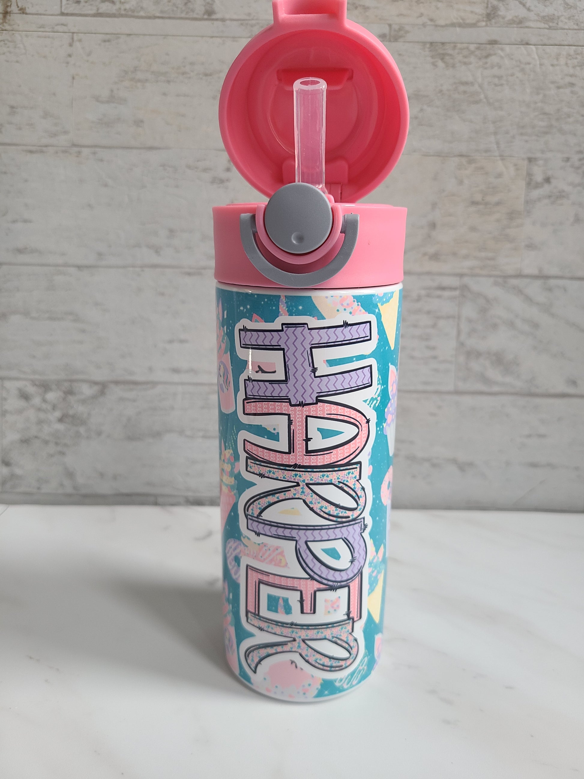 12 oz water bottle with pink lid that has a built-in straw, locking push button and handle. This design features pastel unicorn cupcakes and ice cream cones. Personalized in coordinating colors. Lid is popped open easily to show the silicone straw