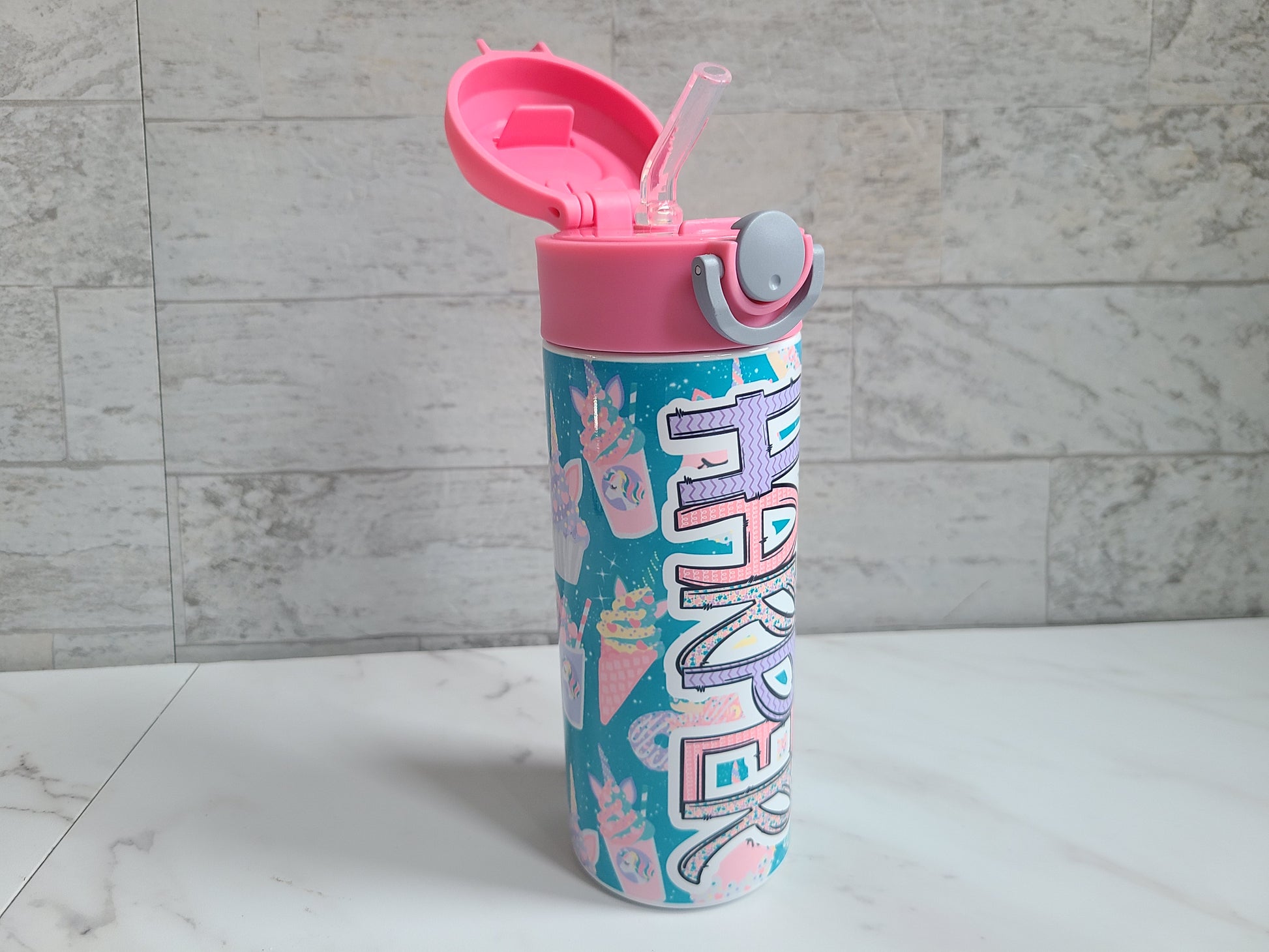 12 oz water bottle with pink lid that has a built-in straw, locking push button and handle. This design features pastel unicorn cupcakes and ice cream cones. Personalized in coordinating colors. Lid is popped open easily to show the silicone straw