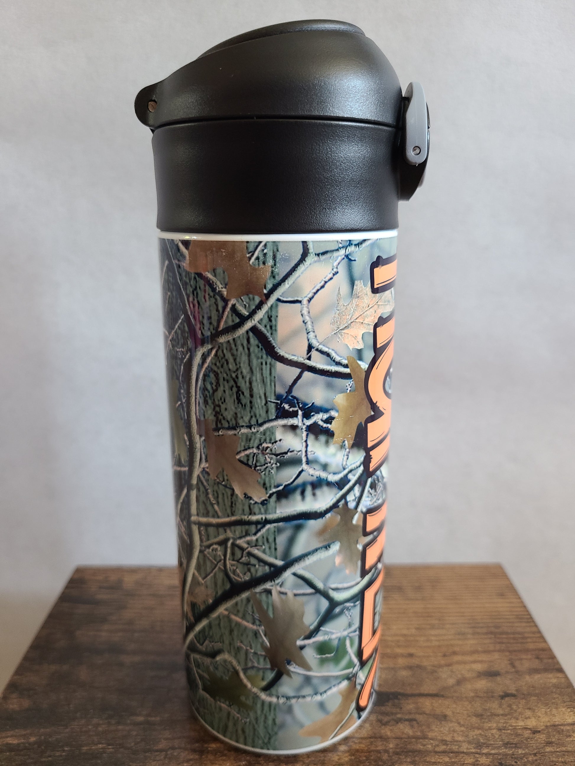 12 oz water bottle with a black lid that has a built-in straw, locking push button and handle. This design features real tree camo with orange personalization. Back to School.