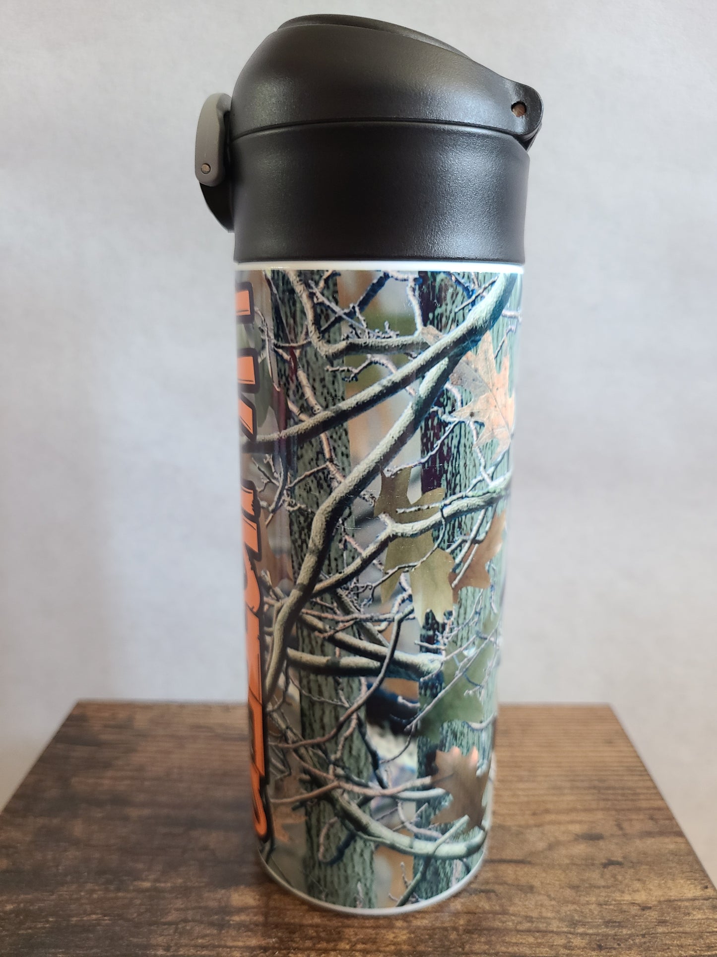 12 oz water bottle with a black lid that has a built-in straw, locking push button and handle. This design features real tree camo with orange personalization. Back to School.