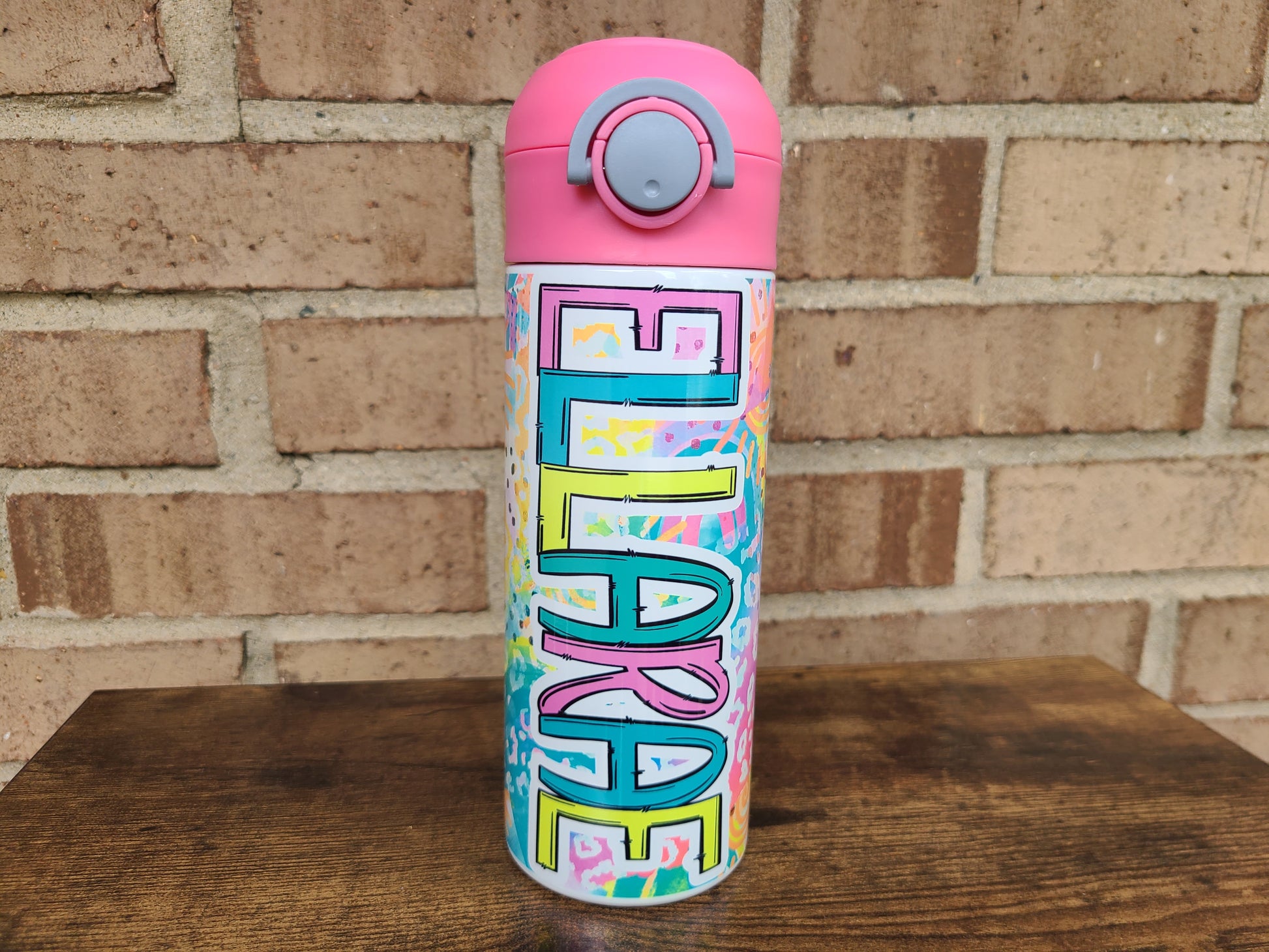 12oz water bottle with pink lid that has a built in straw, locking push button and handle. This design features bright colored animal print with sunshine and rainbows. Personalized in coordinating bright colors with a pink lid. Back to school.