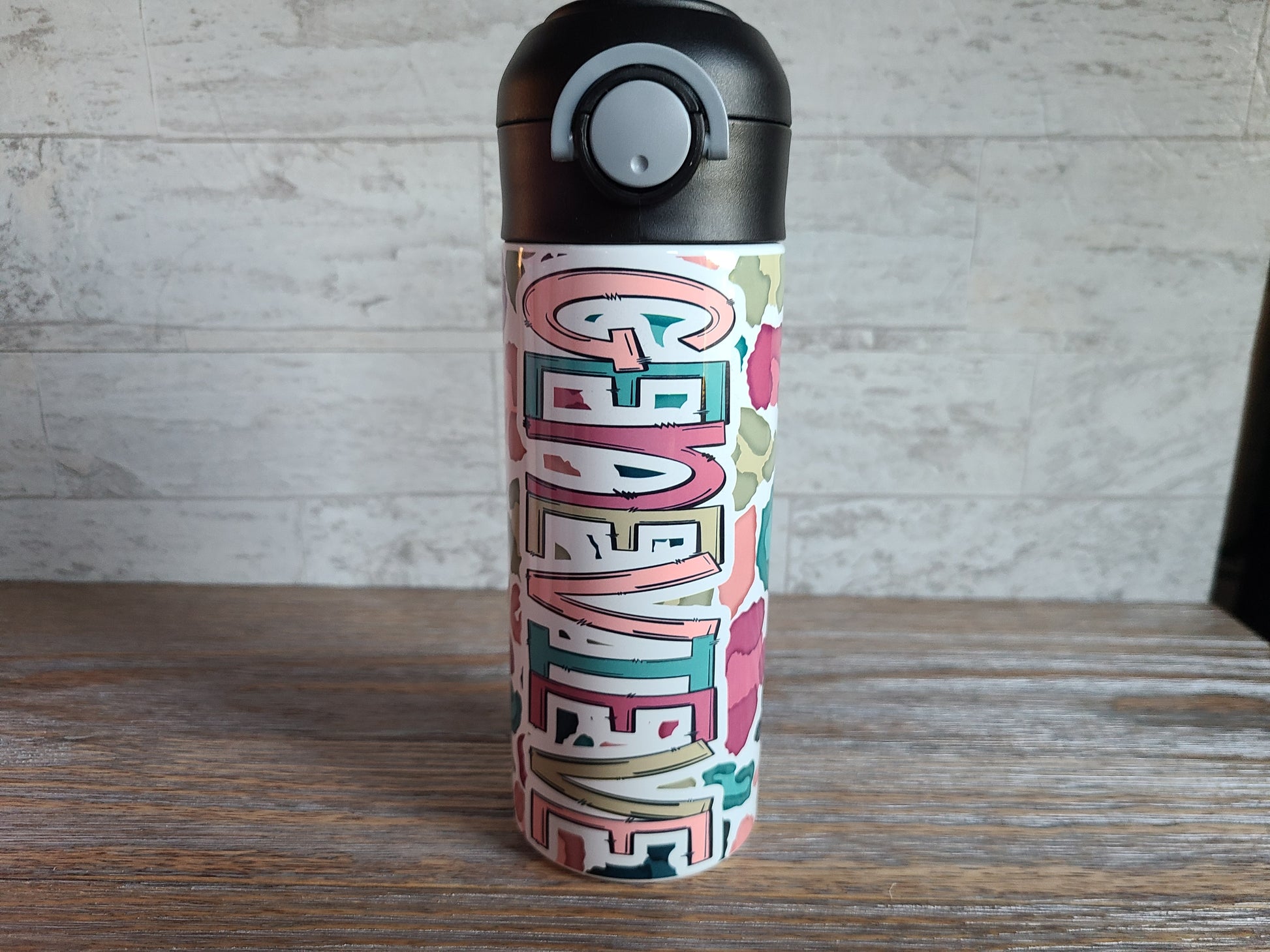  12 oz water bottle with a black lid that has a built-in straw, locking push button and handle. This design features a white background multi-colored leopard print. Personalized in coordinating colors. Back to School.