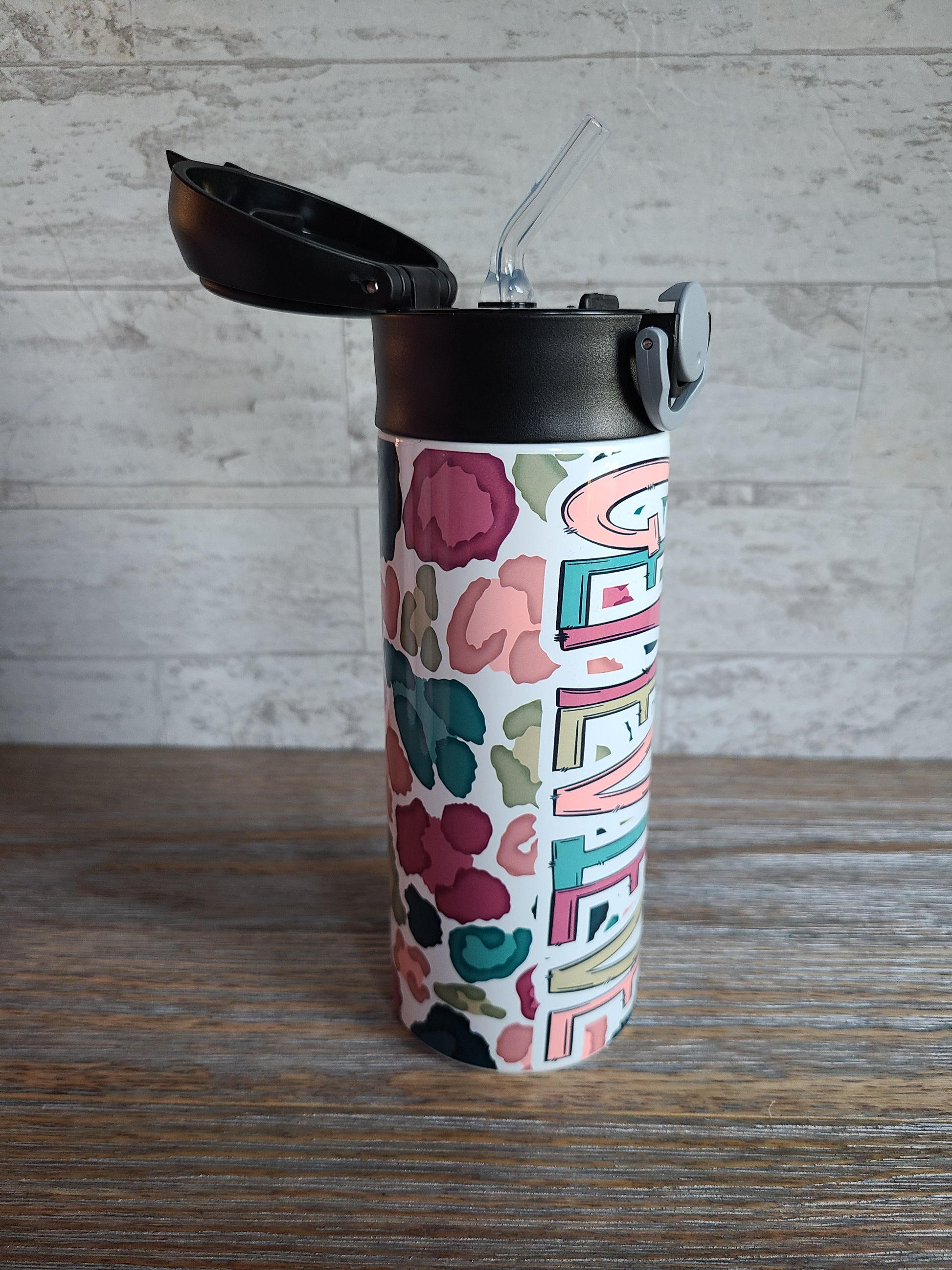  12 oz water bottle with a black lid that has a built-in straw, locking push button and handle. This design features a white background multi-colored leopard print. Personalized in coordinating colors. Lid is popped open easily to show the silicone straw