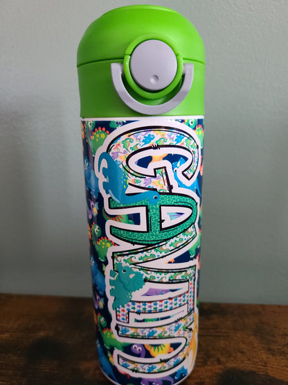 12 oz water bottle with flip top and built in straw. Colorful dinosaur themed water bottle for kids. Back to school water bottle for kids. Dinosaurs in yellow, green, purple and blue with navy blue background and green lid.