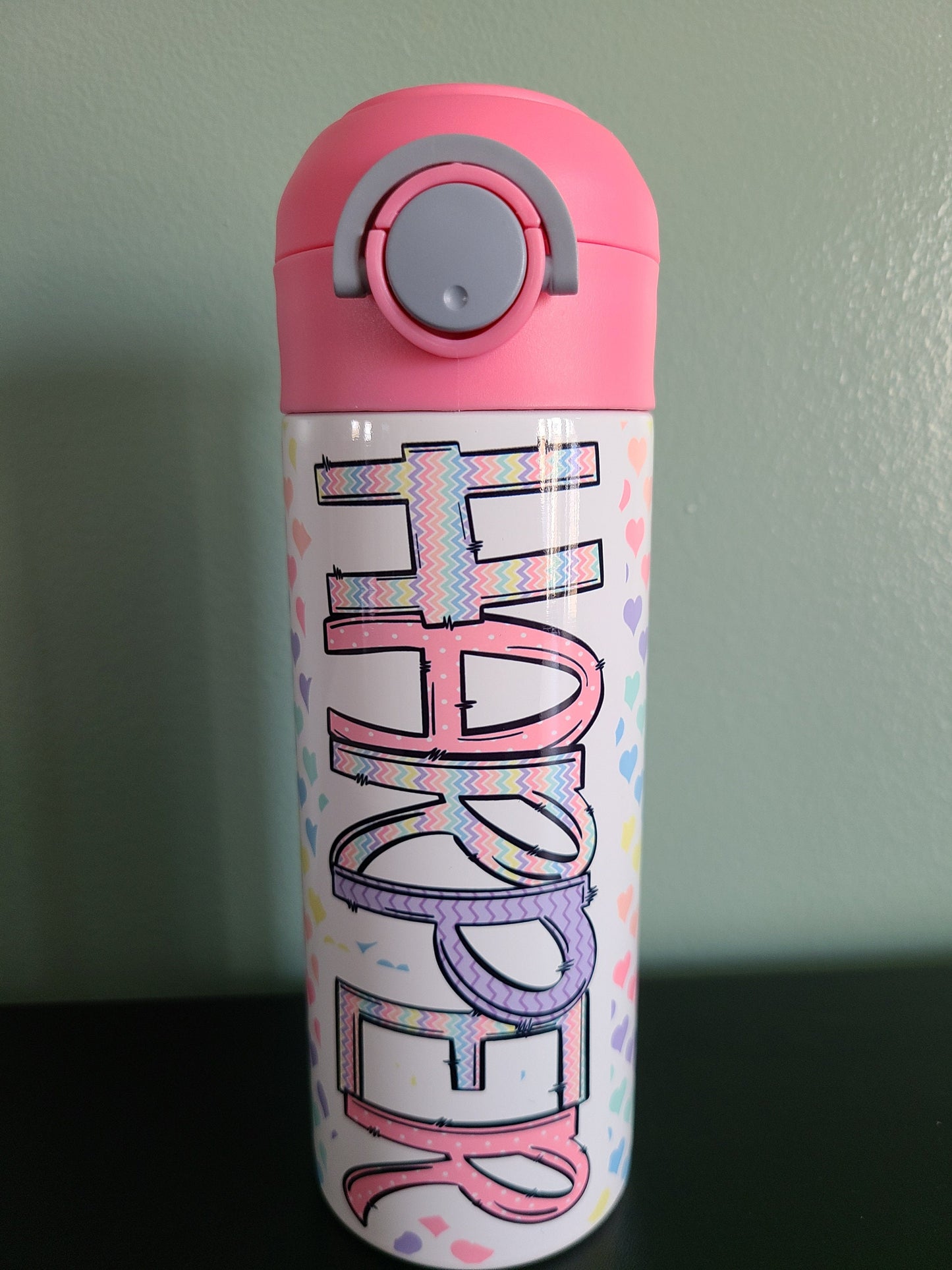 12 oz water bottle with flip top and built in straw. Pastel colored heart themed water bottle for kids. Back to school water bottle for kids. Hearts in pastel colors with a complimentary design personalization and pink lid.