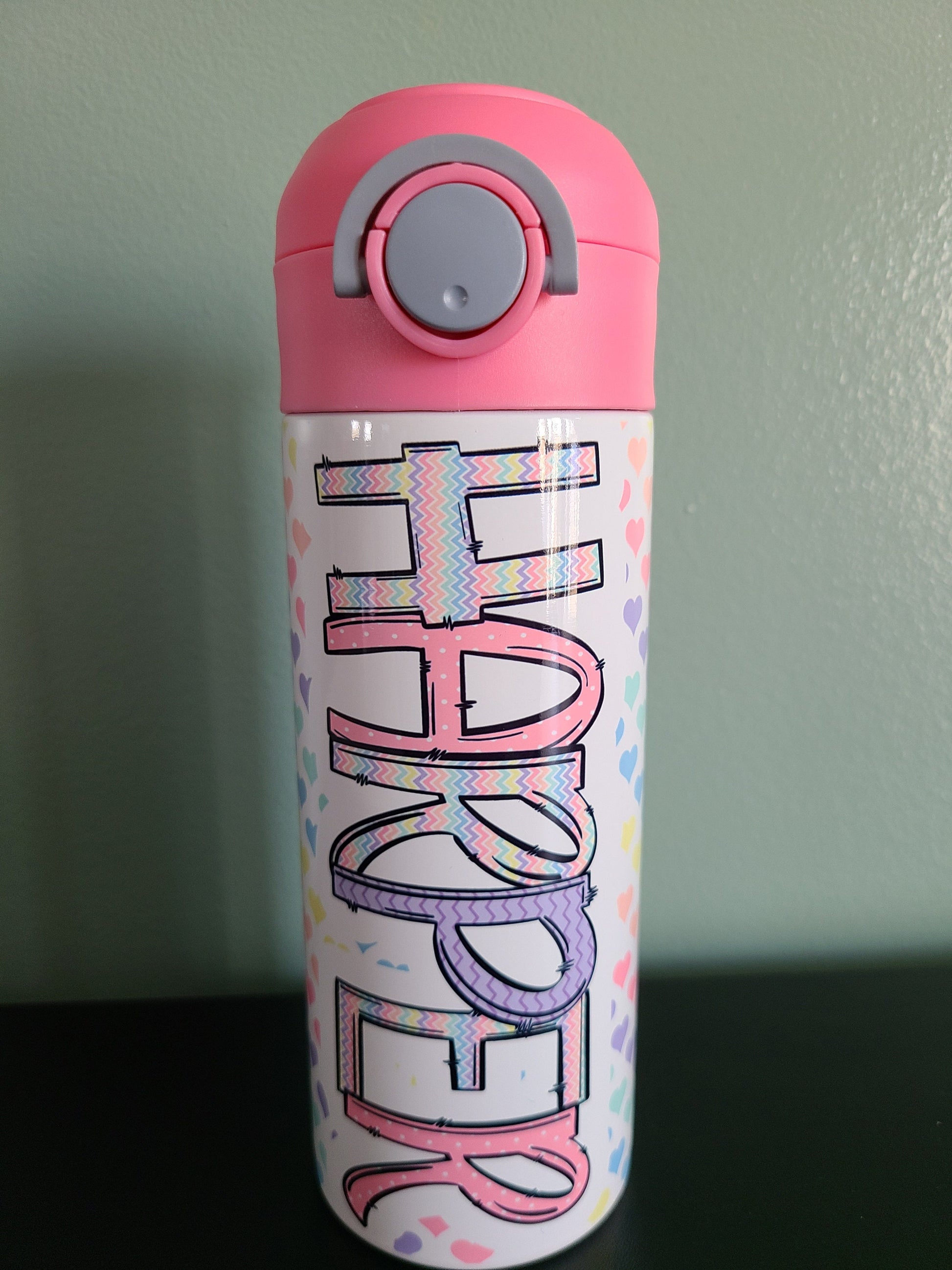 12 oz water bottle with flip top and built in straw. Pastel colored heart themed water bottle for kids. Back to school water bottle for kids. Hearts in pastel colors with a complimentary design personalization and pink lid.