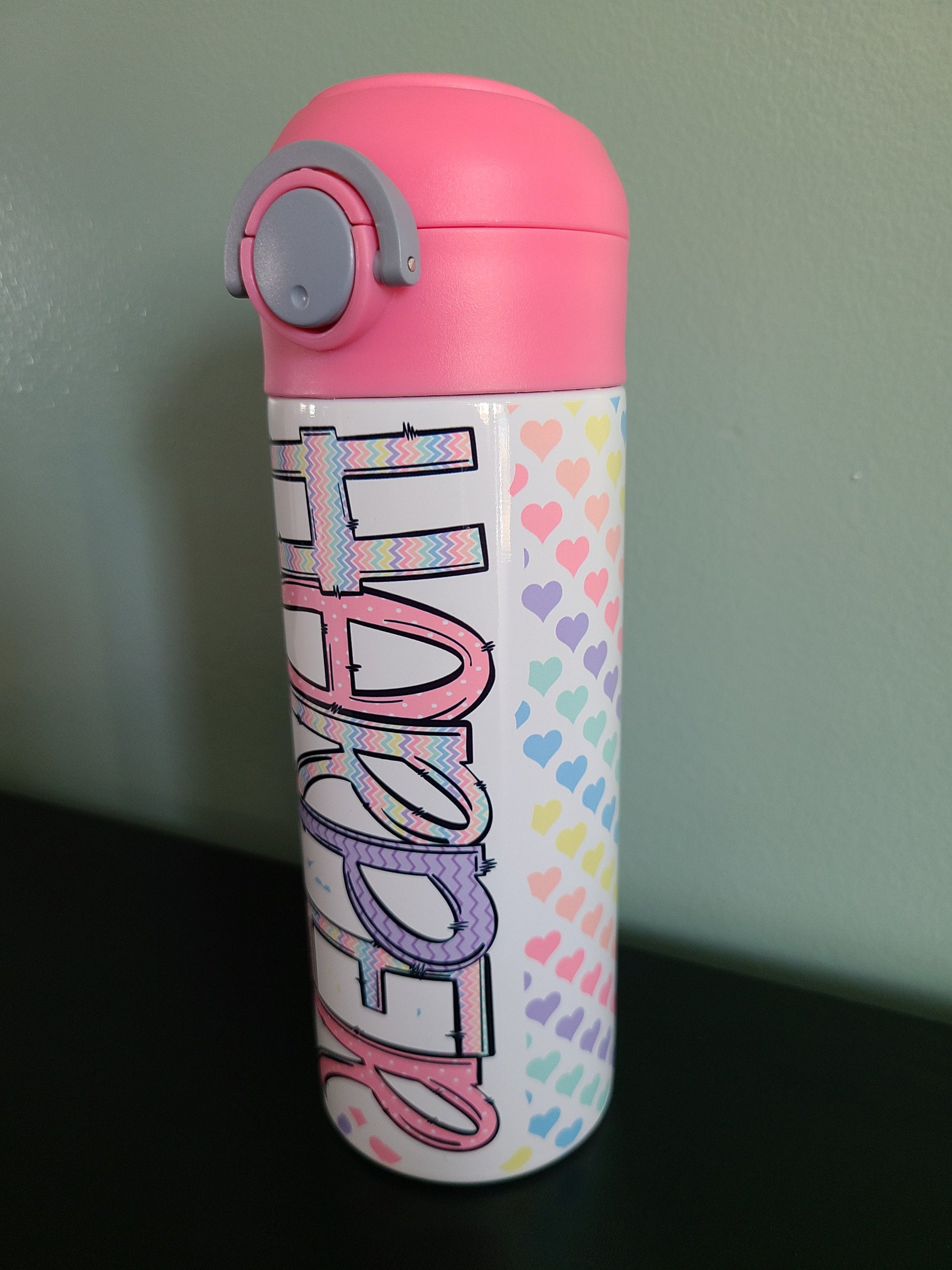 12 oz water bottle with flip top and built in straw. Pastel colored heart themed water bottle for kids. Back to school water bottle for kids. Hearts in pastel colors with a complimentary design personalization and pink lid.