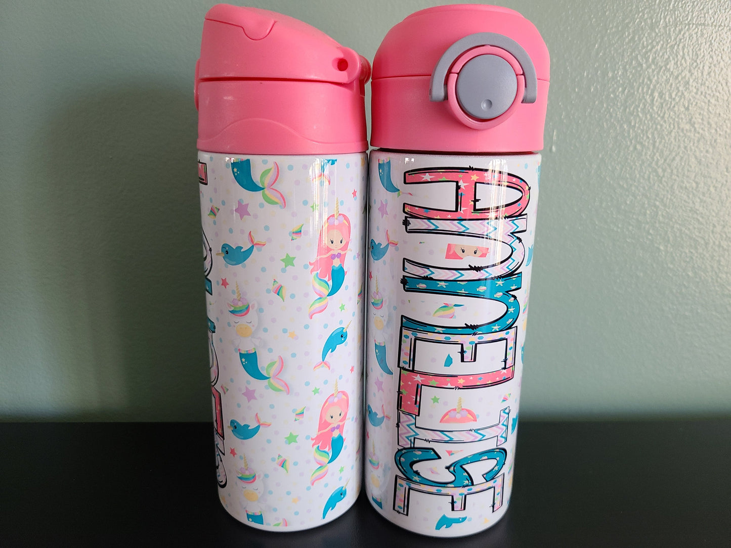 12 oz water bottle with a pink lid that has a built-in straw, locking push button and handle. This design featuring mermaids and unicorns. Personalized in coordinating colors. Back to School. two bottles to show the front and back