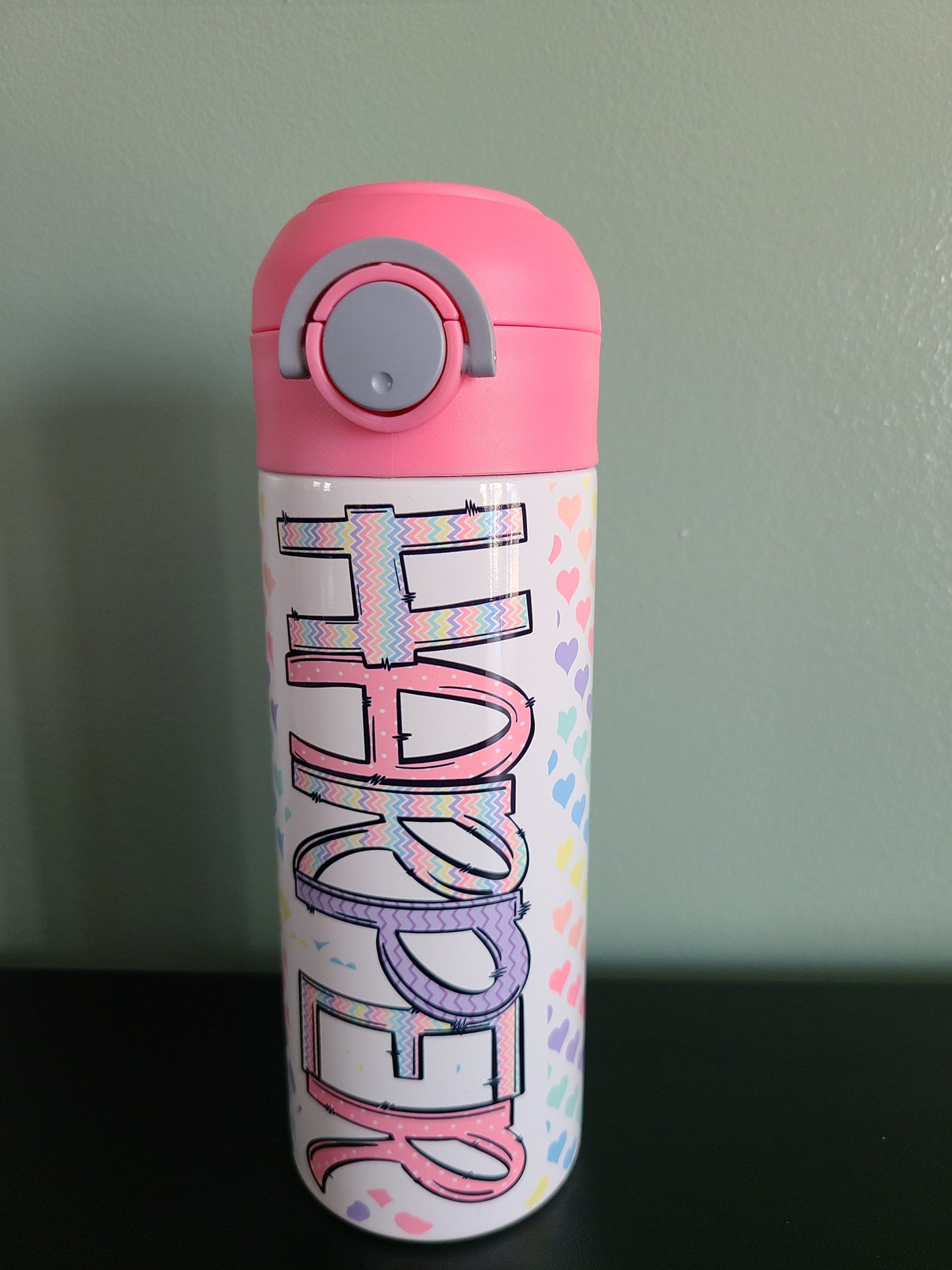 12 oz water bottle with flip top and built in straw. Pastel colored heart themed water bottle for kids. Back to school water bottle for kids. Hearts in pastel colors with a complimentary design personalization and pink lid.