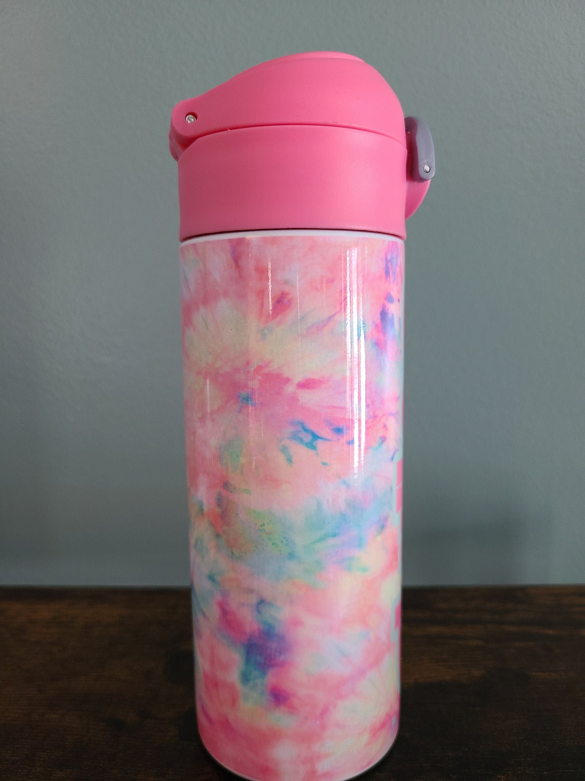 12 oz water bottle with flip top and built in straw. Pink tie dye themed water bottle for kids. Back to school water bottle for kids. Tie dye in pastel colors with a name in pink and pink lid.